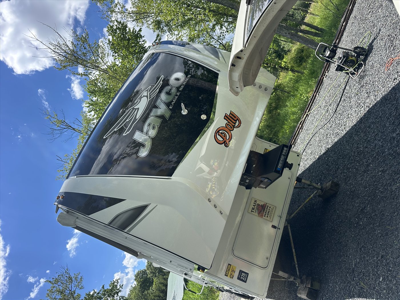 Jayco Eagle Series fifth-wheel front cap with custom Dolly decal after exterior detail — glossy white fiberglass reflecting sky and trees